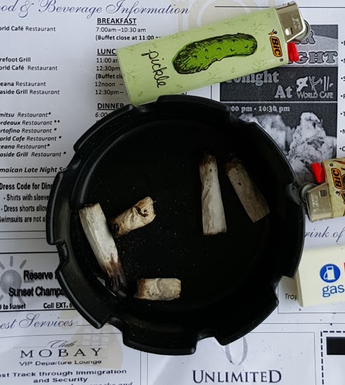 A ashtray with five roaches of various length, and a lighter with a picture of a pickle on it.