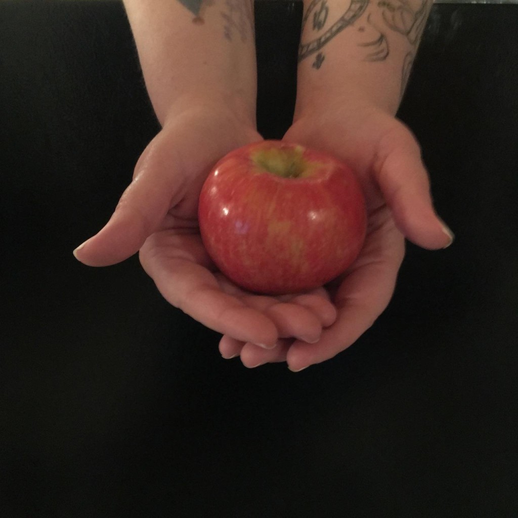 My heavily tattooed hands and arms holding an apple in front of a black background, like the cover of Twilight