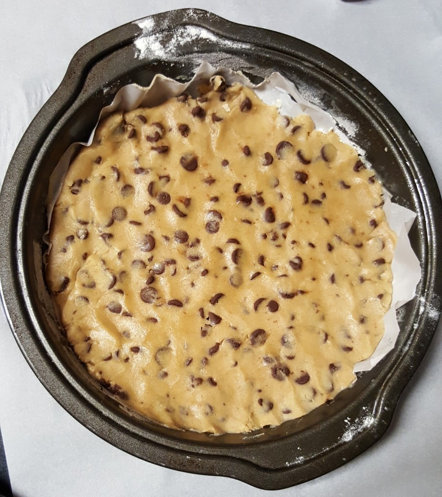 A round cake pan with a layer of chocolate chip cookie dough covering the bottom.