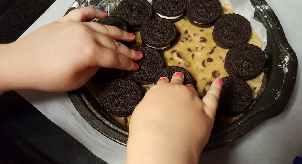 Two adorable little hands pushing Oreos into the cookie dough.