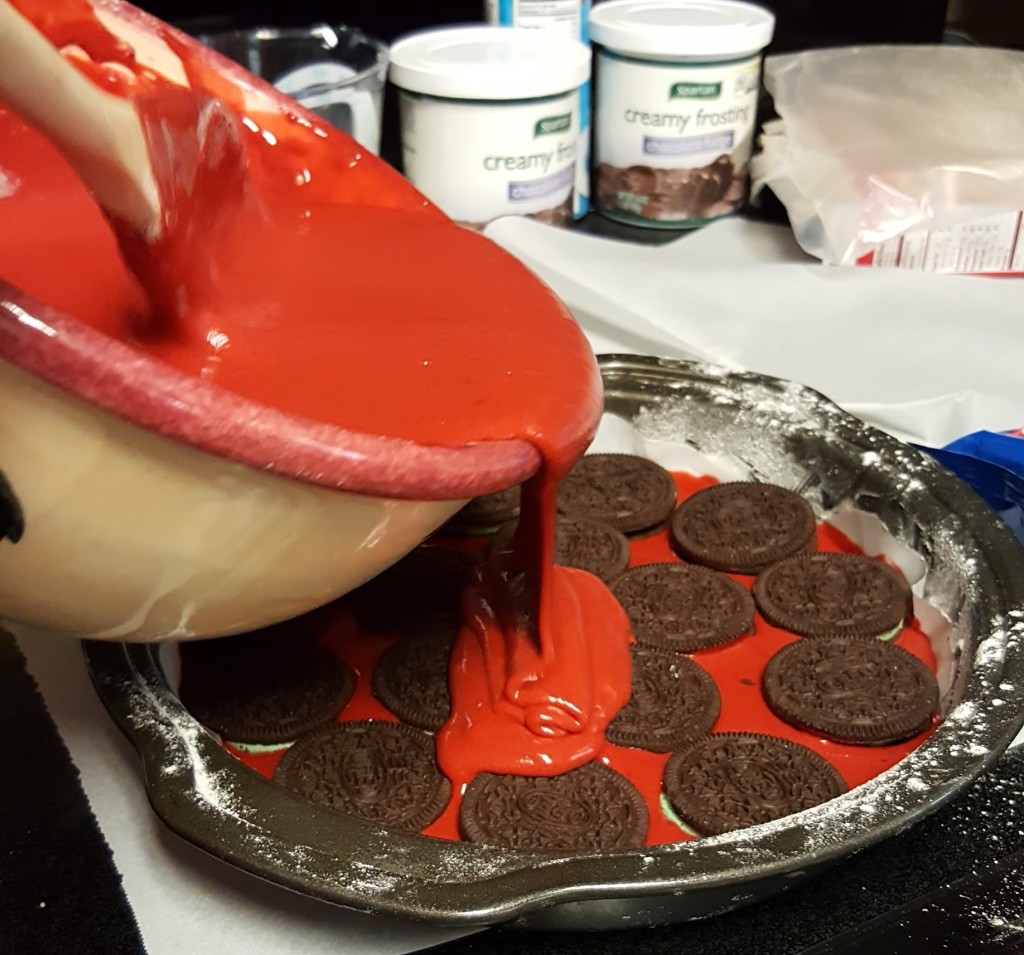 Red Velvet cake batter pouring into a pan and covering a layer of Oreos.