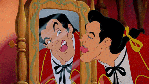A gif of Gaston from the animated Beauty and The Beast. He's licking his teeth clean in a mirror.