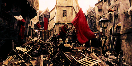 A scene from Les Miserables where Enjolras plants a giant red flag atop the barricade.