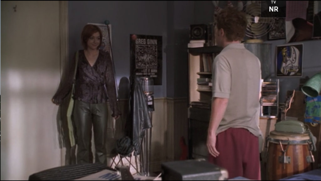 Willow is wearing gray leather pants and a purple-ish wrap shirt with frilly sleeves.