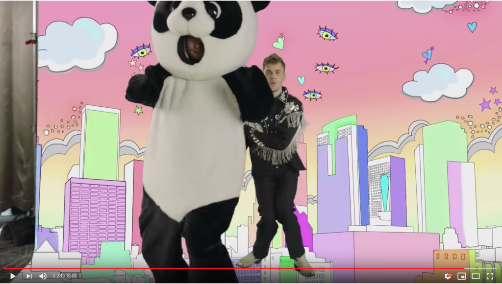 Miserable Panda Ed and Cowboy Beeber are dancing in front of a pink sky background with a pastel city scape as eyes and hearts fly through the sky.