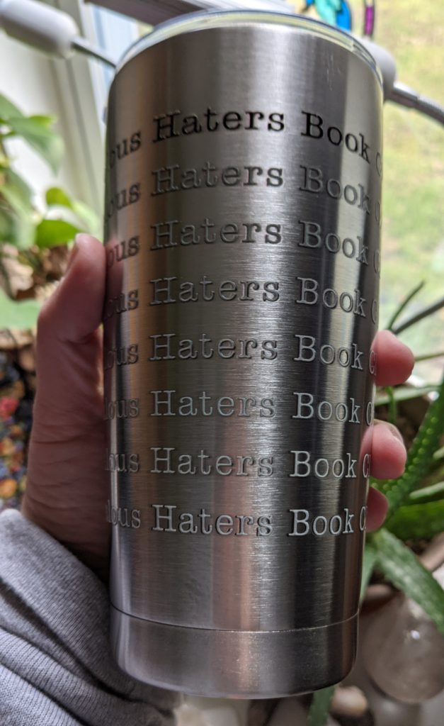 my hand holding a stainless steel tumbler with the words "Jealous Haters Book Club" repeated on it in various shades of gray