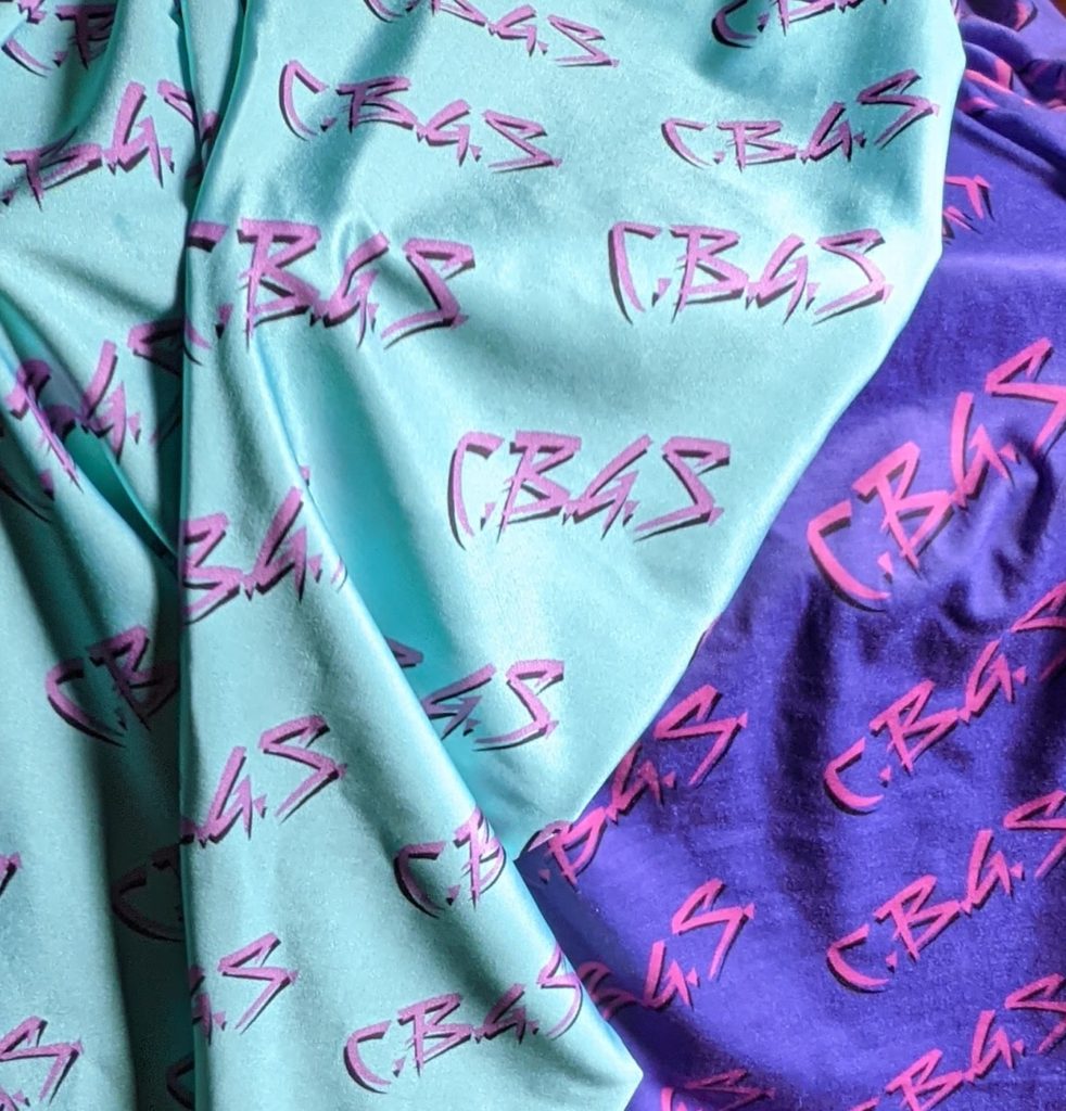 bright turquoise fabric over purple fabric. Both pieces have "C.B.G.S."  in an '80s-esque font in hot pink.